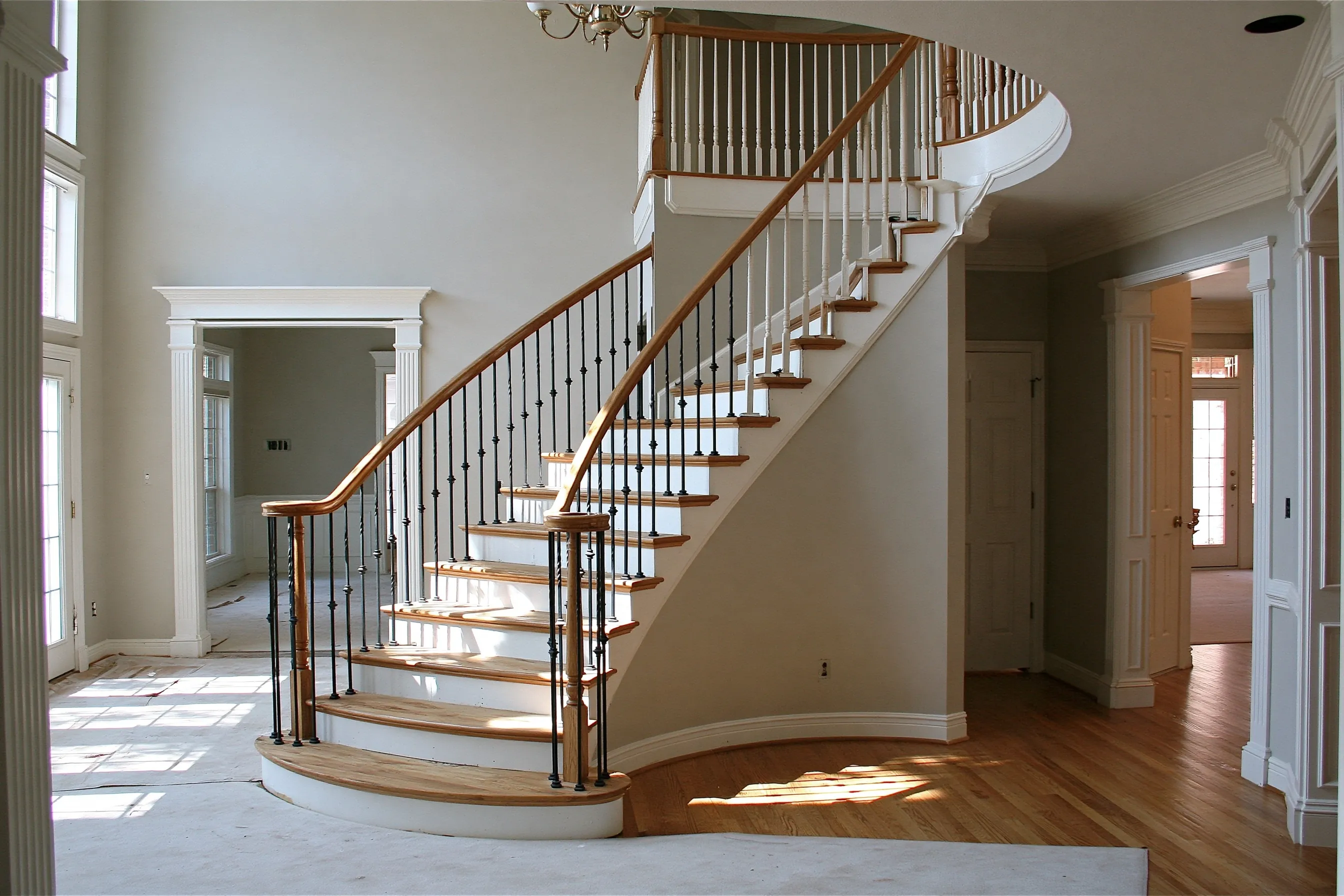 Curved stair mid-update, with black iron balusters on the lower part and white wood spindles still on the upper part