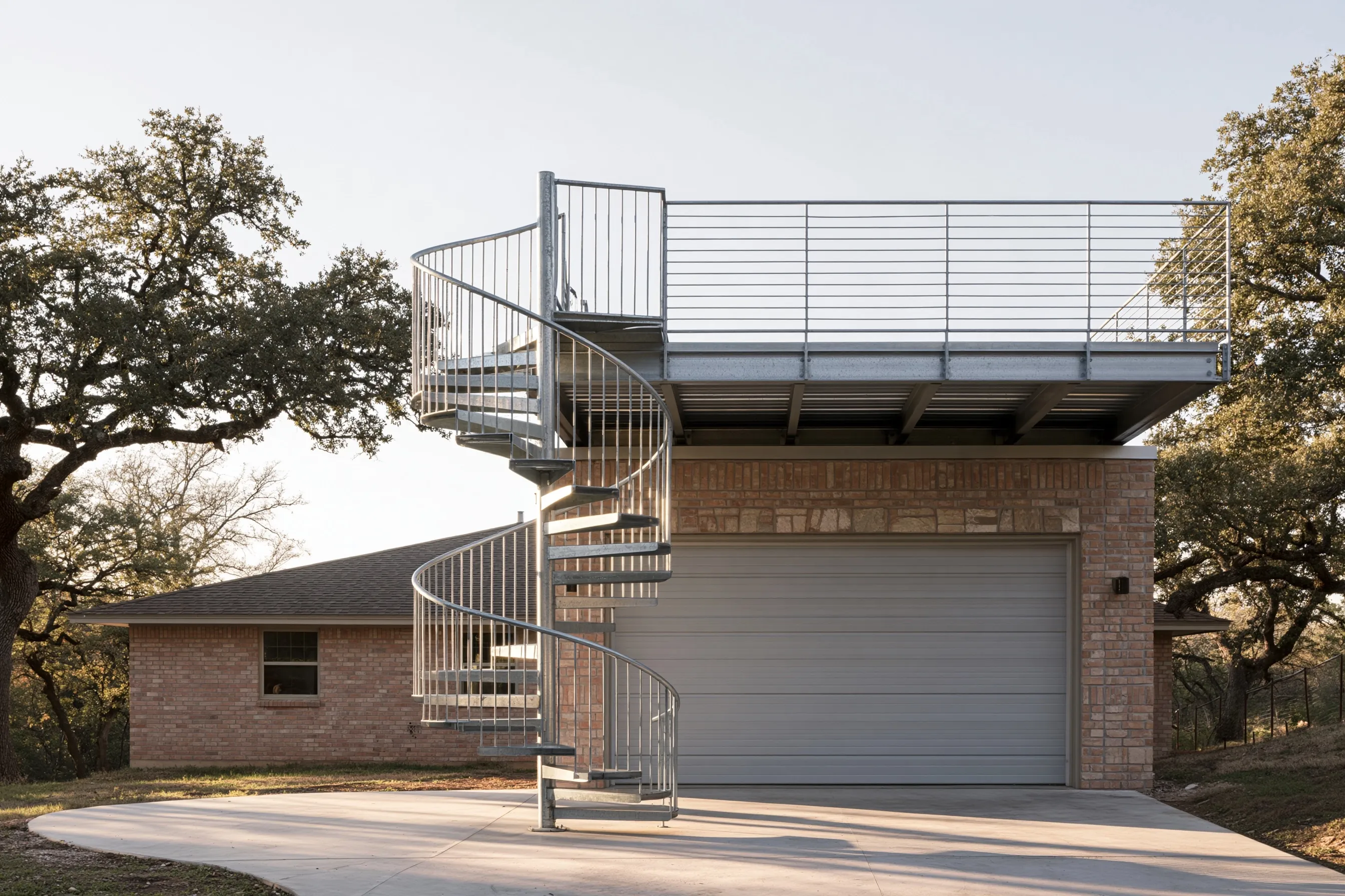 Galvanized steel spiral stair beside a garage door, rising to a steel roof deck with a rod railing on a brick ranch house